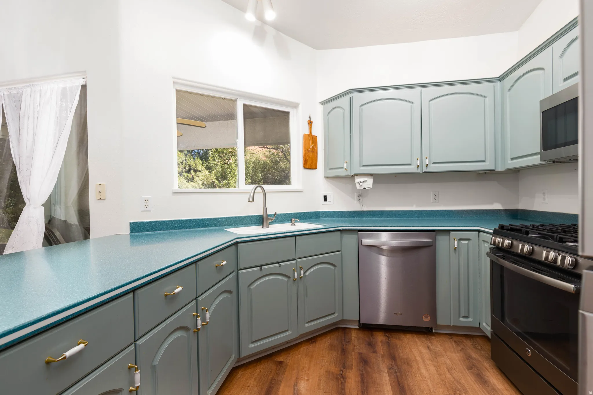 Kitchen featuring wood-finish flooring, light blue cabinetry, a stainless steel dishwasher, and a black range