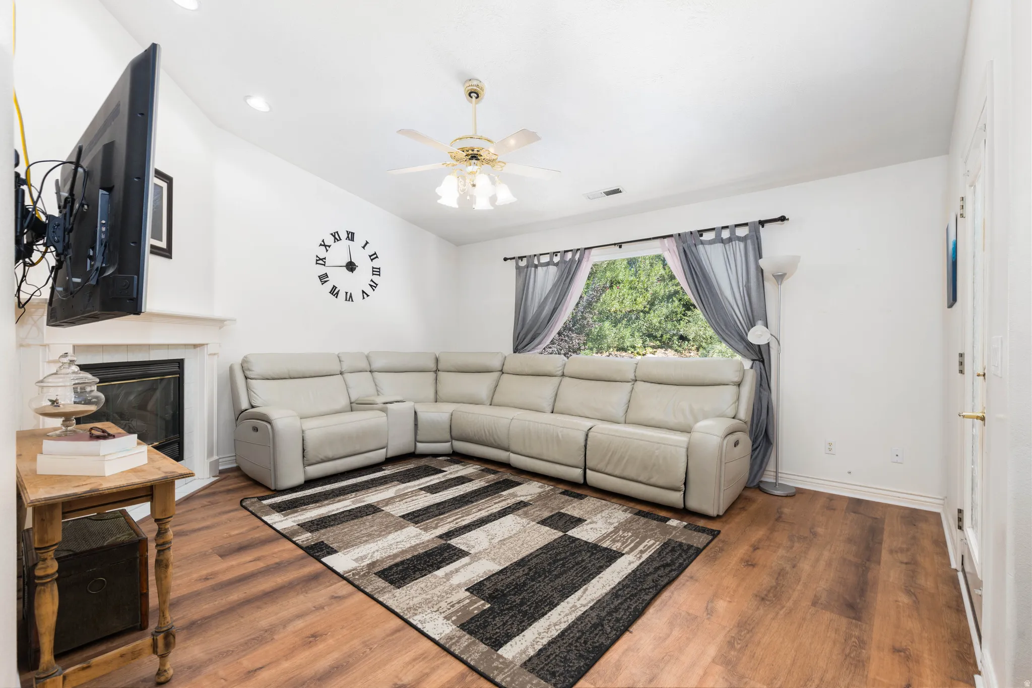 Living area featuring wood-finish flooring, a white fireplace with a mantel, vaulted ceilings, and a ceiling fan with integrated lighting