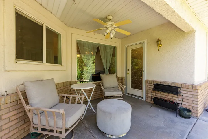 Covered patio with a ceiling fan, brick detailing, a glass-panel door, and an exterior wall lantern