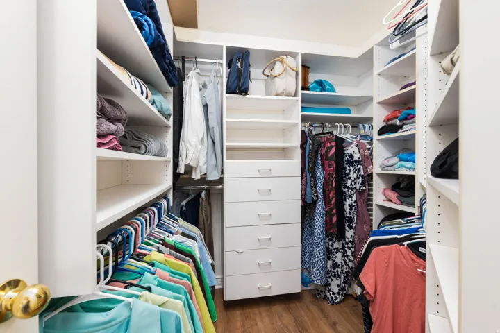 Walk-in closet featuring wood-finish flooring, built-in white shelving, multiple hanging rods, and a built-in drawer unit