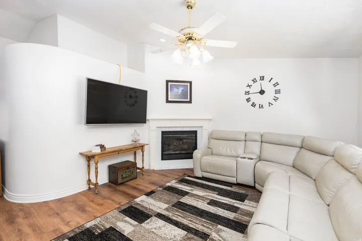 Corner fireplace with a white mantel, wood-finish flooring, and a ceiling fan with integrated lighting