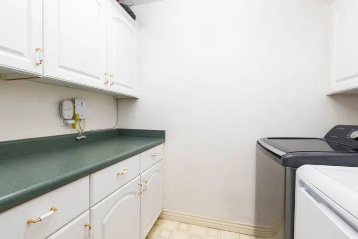 White cabinetry with gold-tone hardware, green countertop, and textured flooring