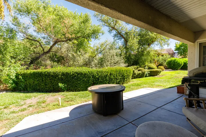 Covered patio with a concrete surface, manicured lawn, and mature trees