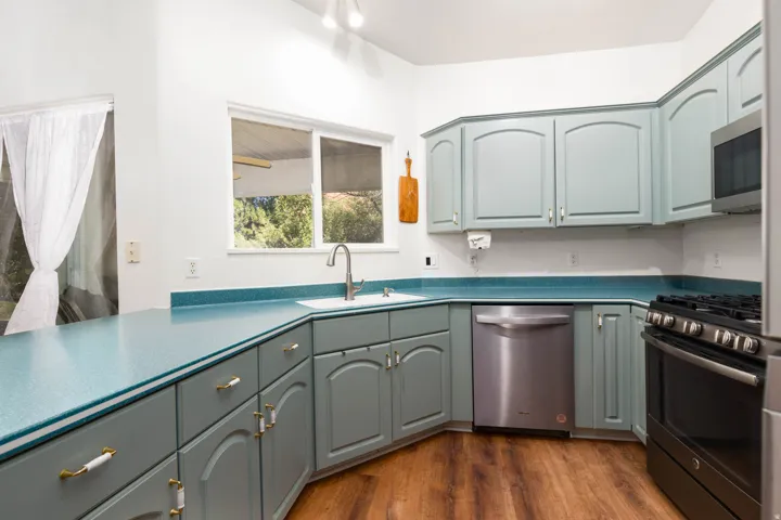 Kitchen featuring wood-finish flooring, light blue cabinetry, a stainless steel dishwasher, and a black range