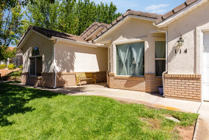Stucco exterior with brick detailing, arched window, attached outdoor lighting, and concrete walkway