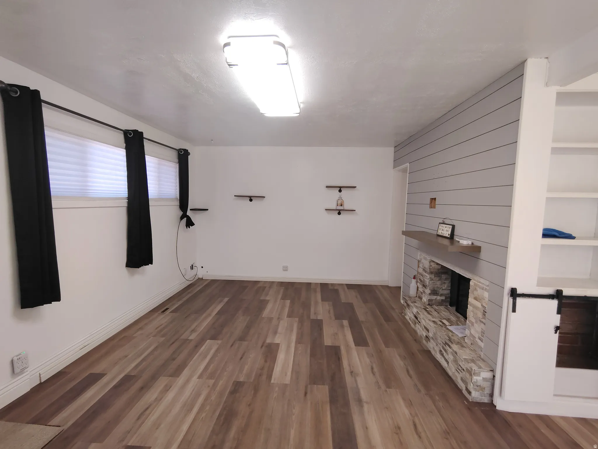 Wood-finish flooring, shiplap accent wall, stone-clad fireplace, integrated shelving, and built-in cabinetry with barn door hardware