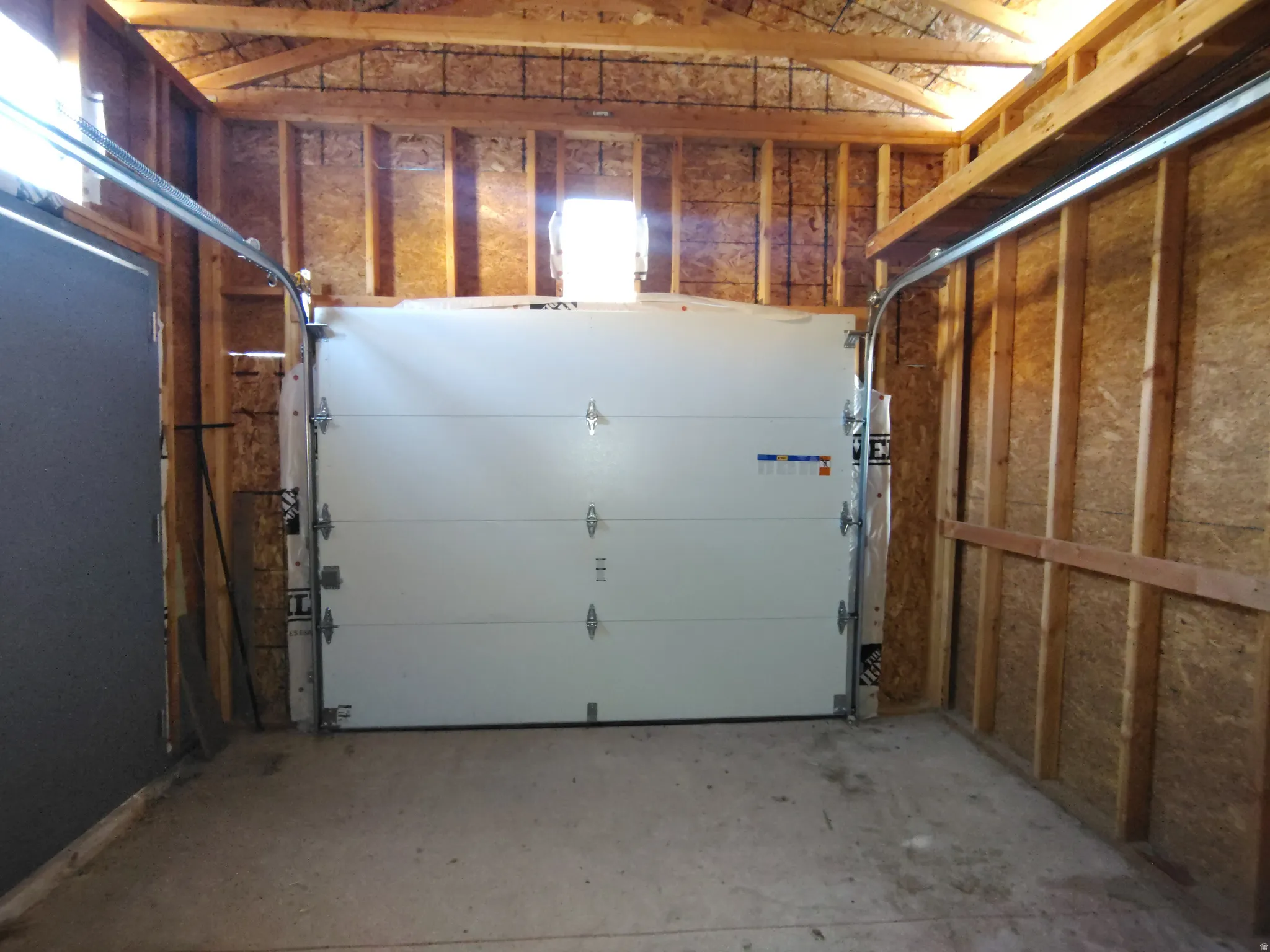 Attached garage with exposed wood framing, concrete flooring, and a white paneled garage door