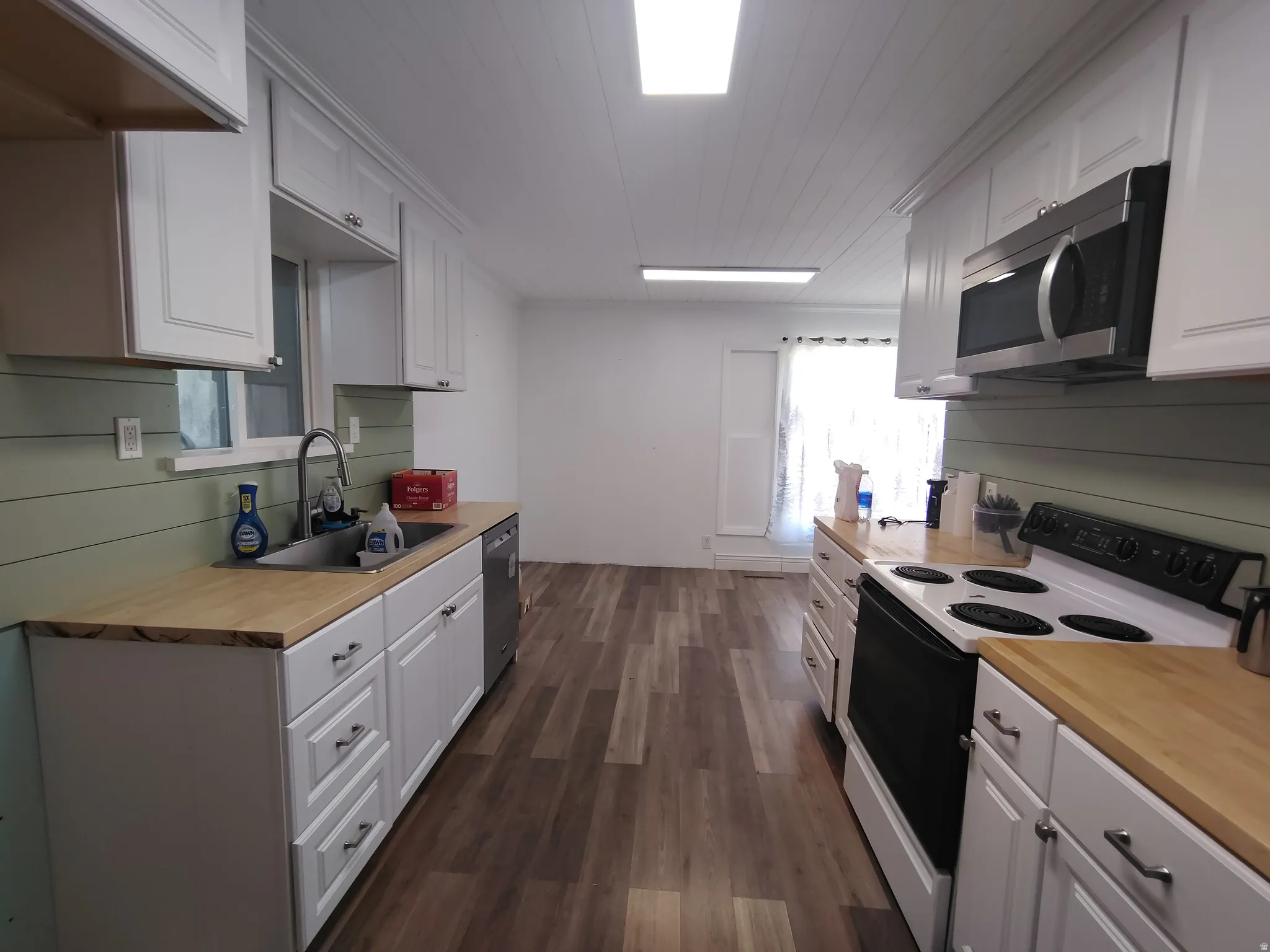 Galley kitchen featuring white cabinetry, light wood-finish countertops, stainless steel appliances, and wood-finish flooring