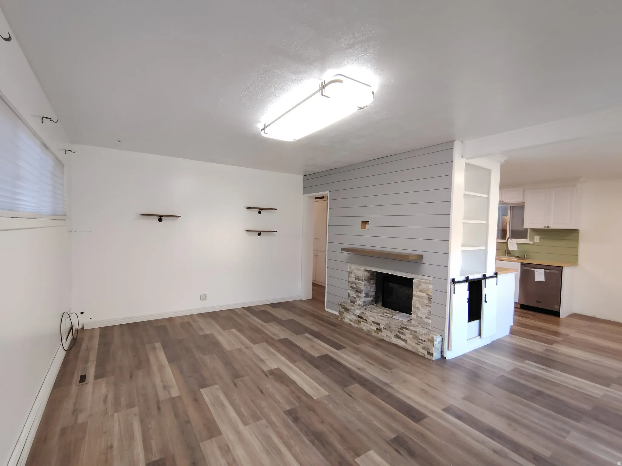 Wood-finish flooring throughout, stone fireplace with a wood mantle, shiplap accent wall, built-in shelving, and recessed lighting