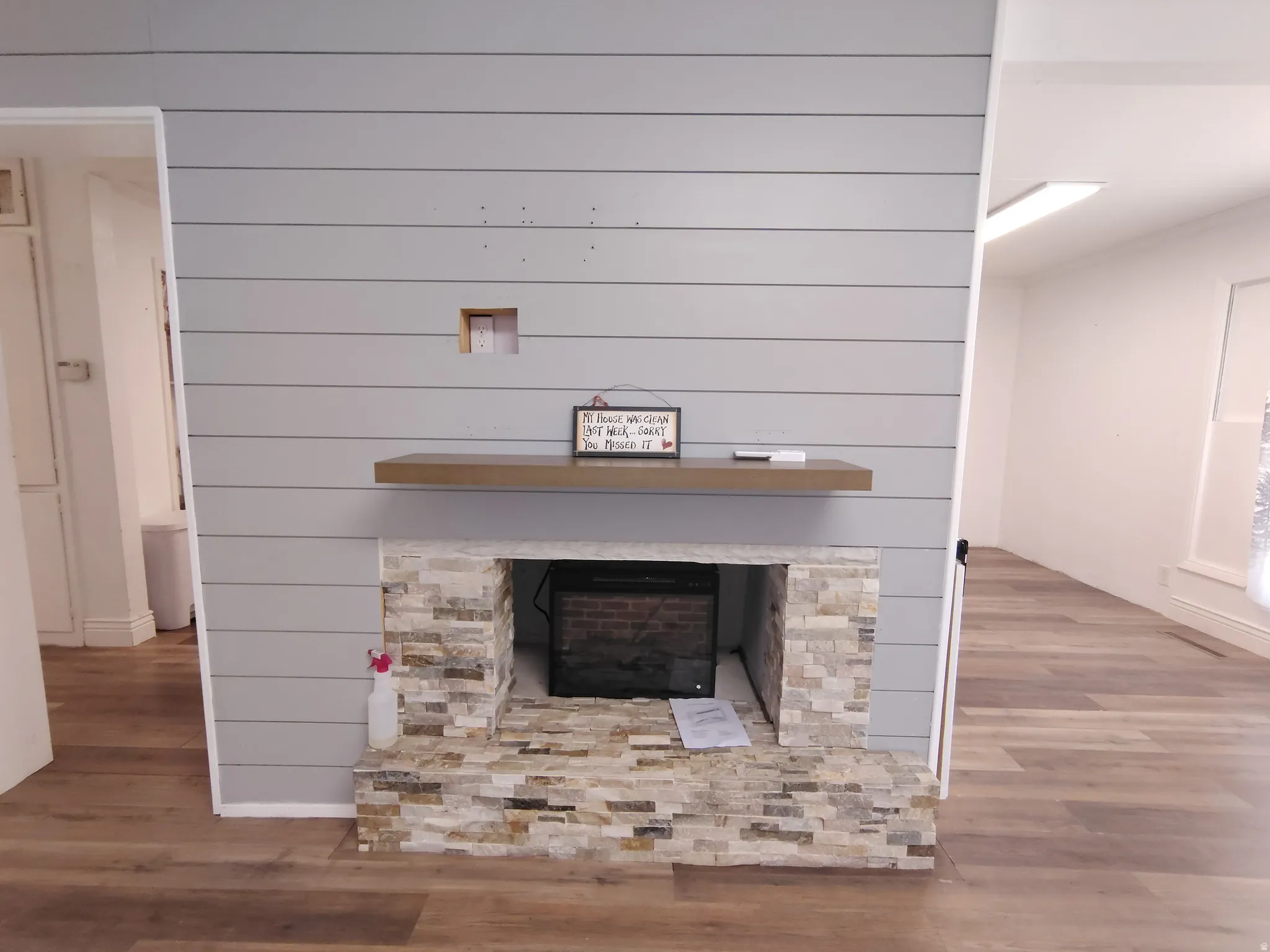 Shiplap accent wall with a stone-clad fireplace and wood-finish flooring
