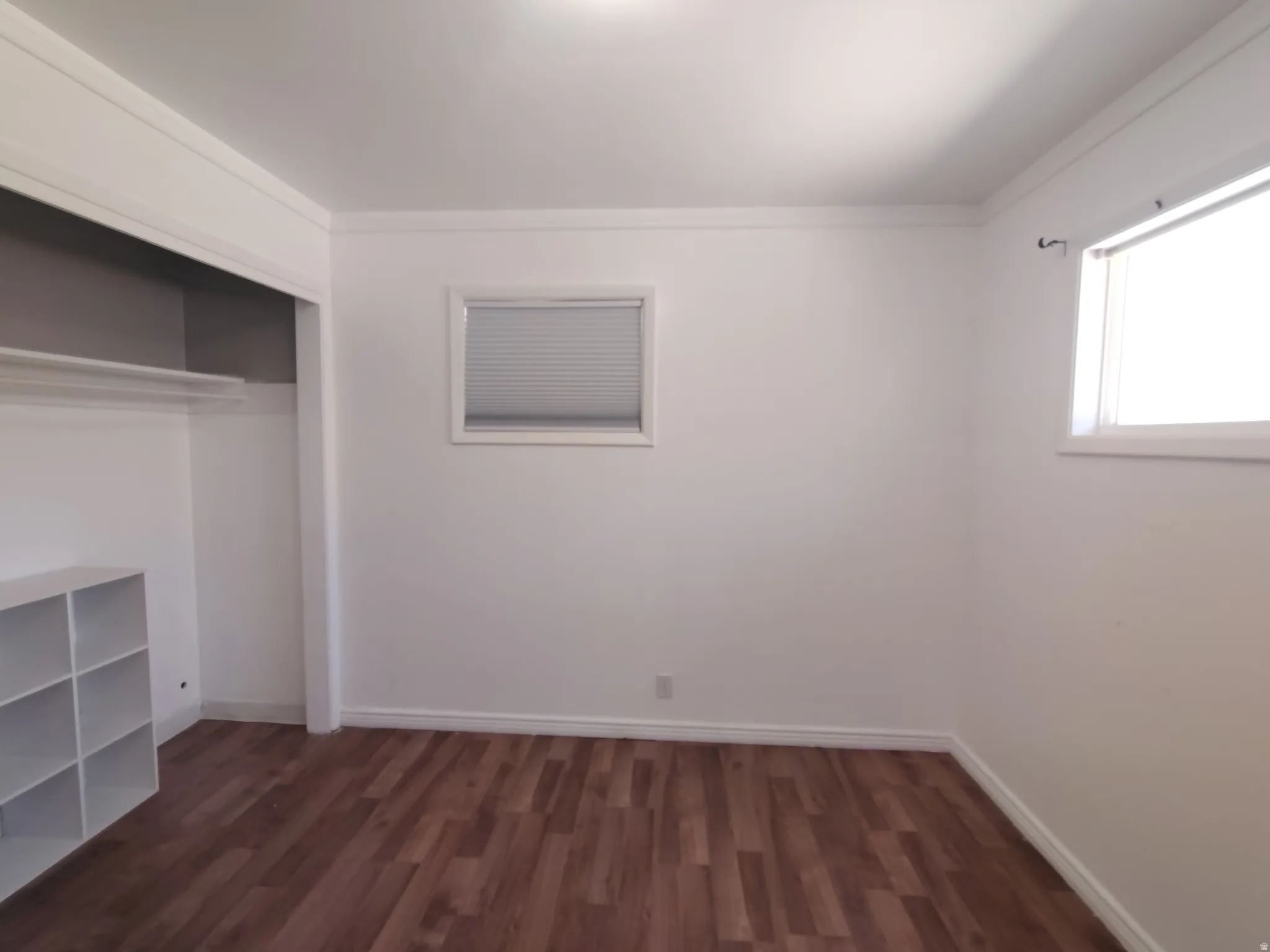 Wood-finish flooring with white baseboards, crown molding, and a built-in closet with shelving