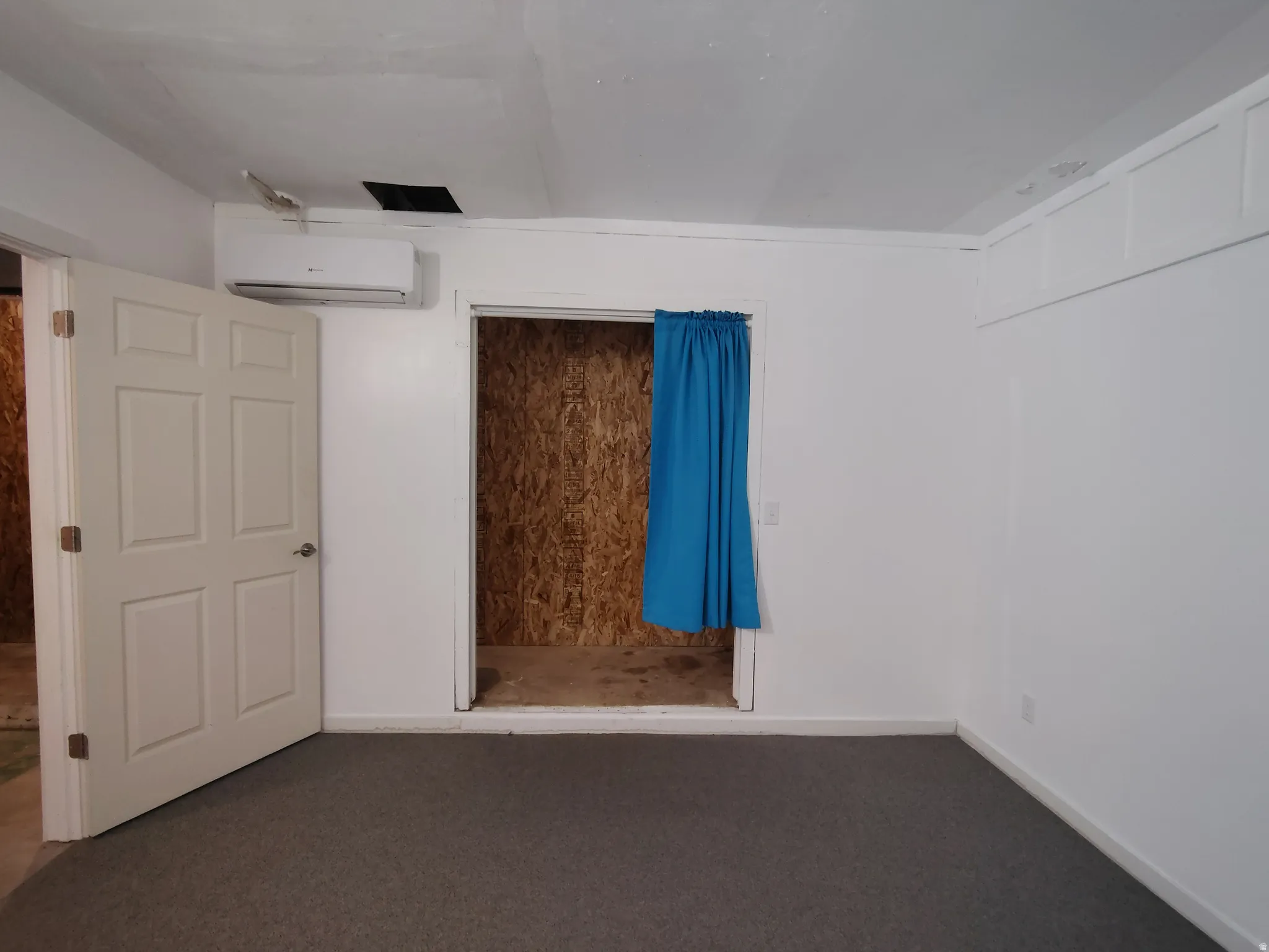 Wall-mounted air conditioning unit, neutral tone carpeting, white paneled interior door, and white walls