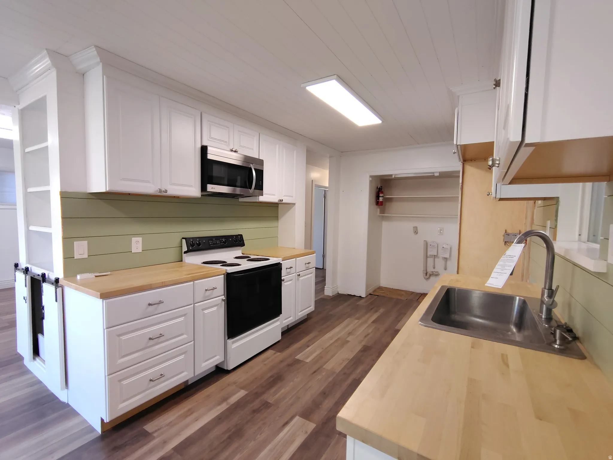 Kitchen featuring wood-finish flooring, white cabinetry, light wood countertops, stainless steel sink, and a green shiplap backsplash