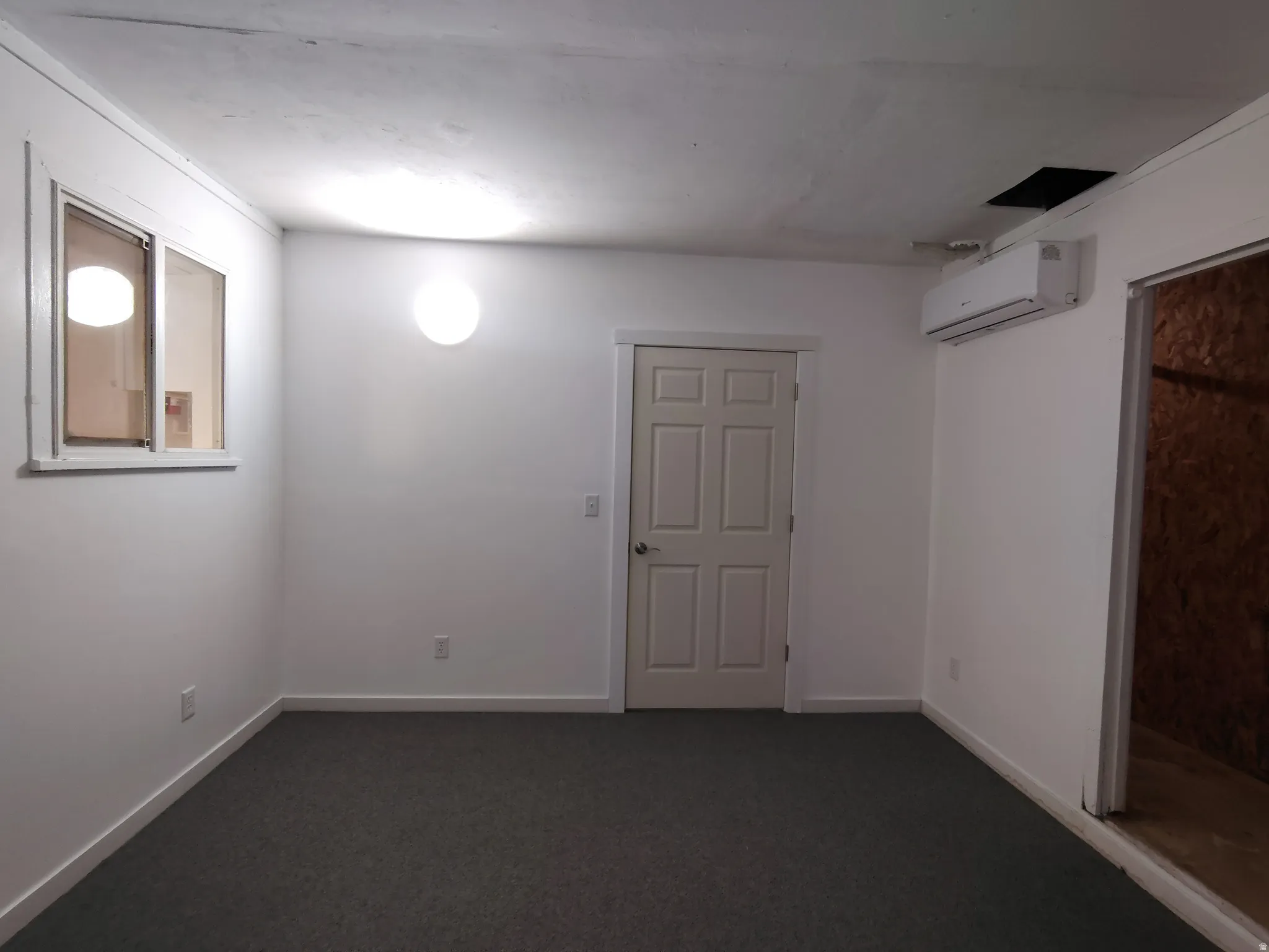 Textured carpet flooring, white painted walls, wall-mounted spherical light fixture, a window with white trim, and a white interior door