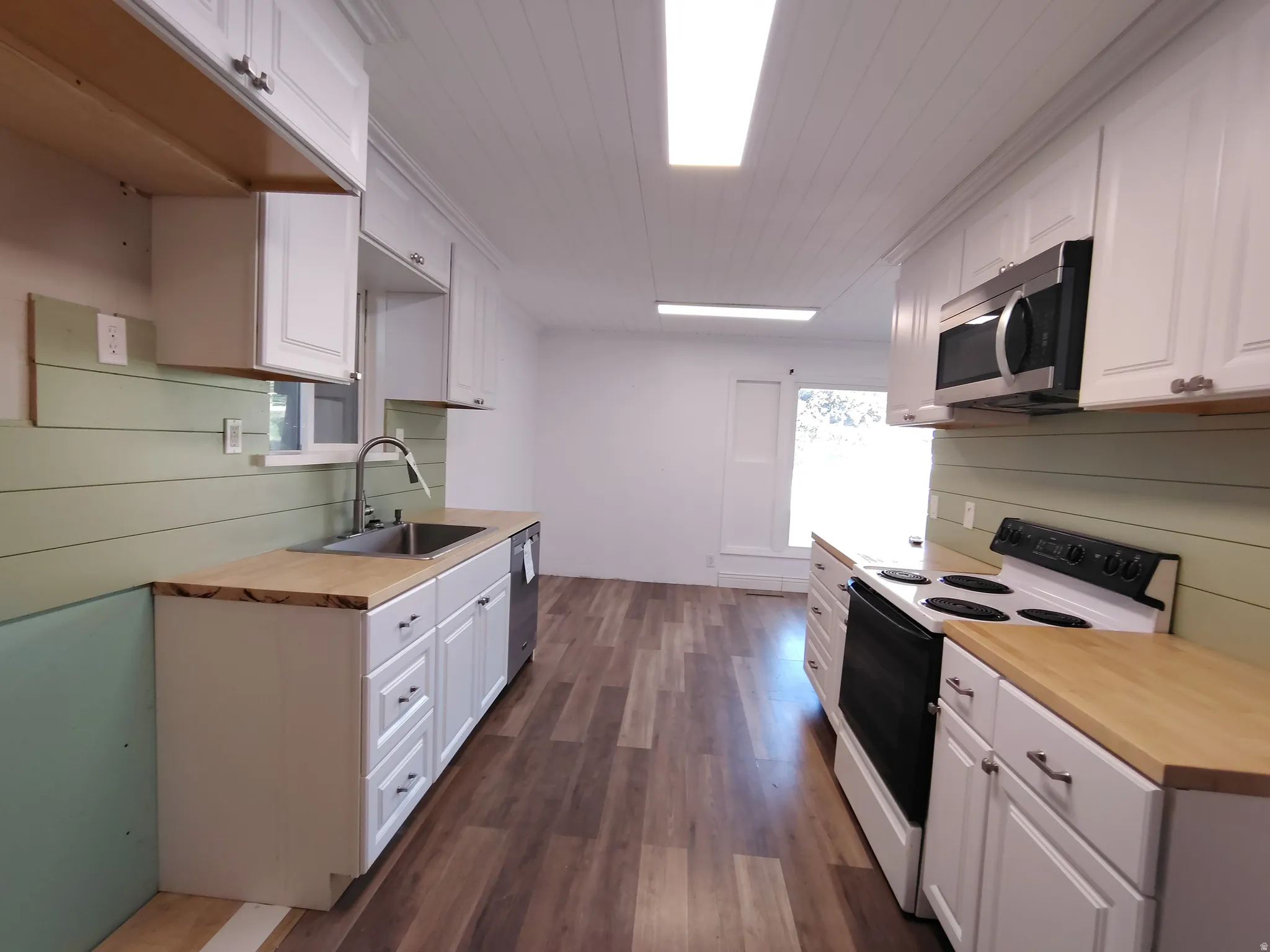 Wood-finish flooring, white cabinetry, light wood countertops, stainless steel sink, and a stainless steel microwave