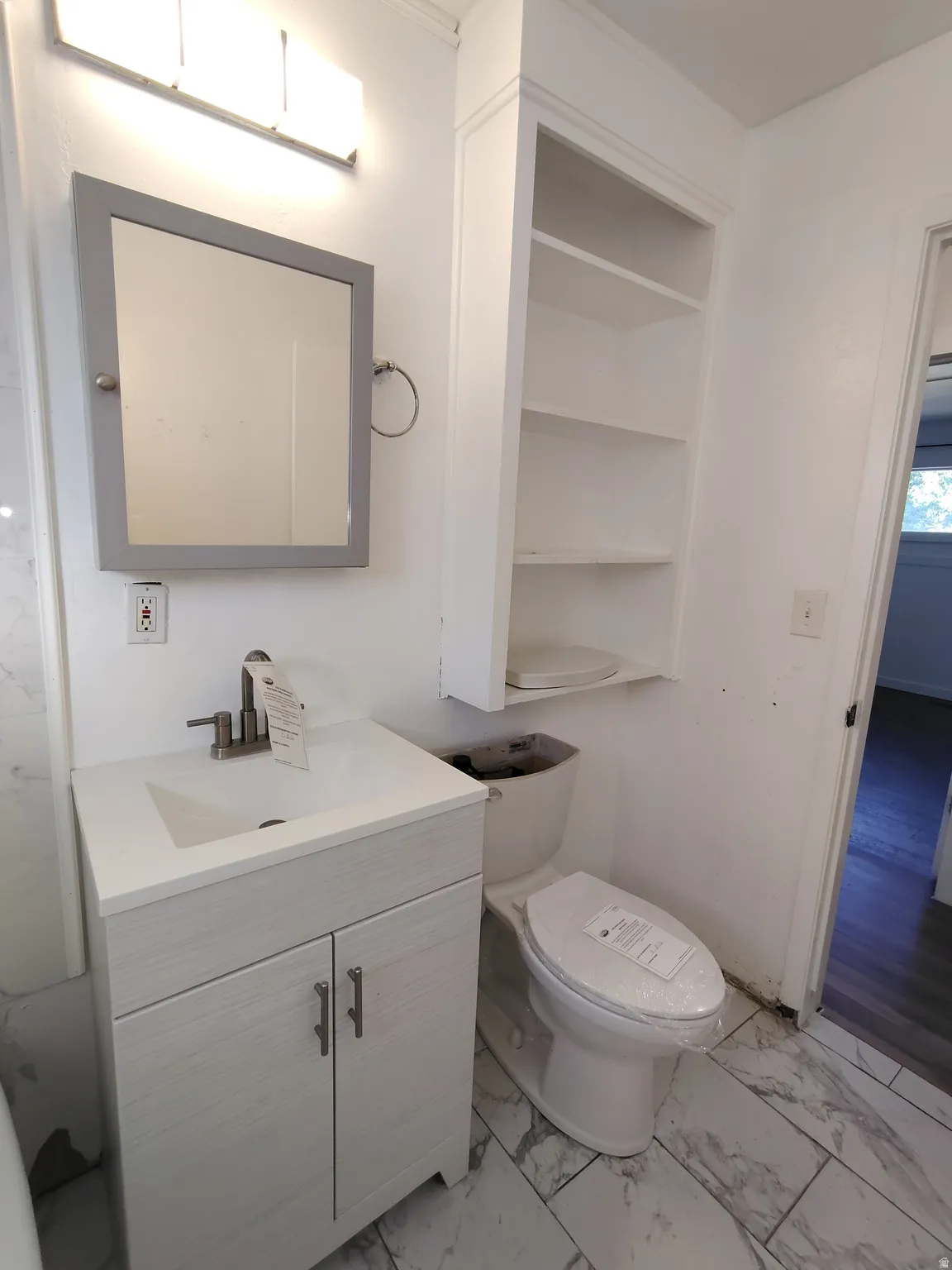 Vanity with integrated sink, wall-mounted mirror, overhead lighting fixture, built-in shelving, and tile flooring
