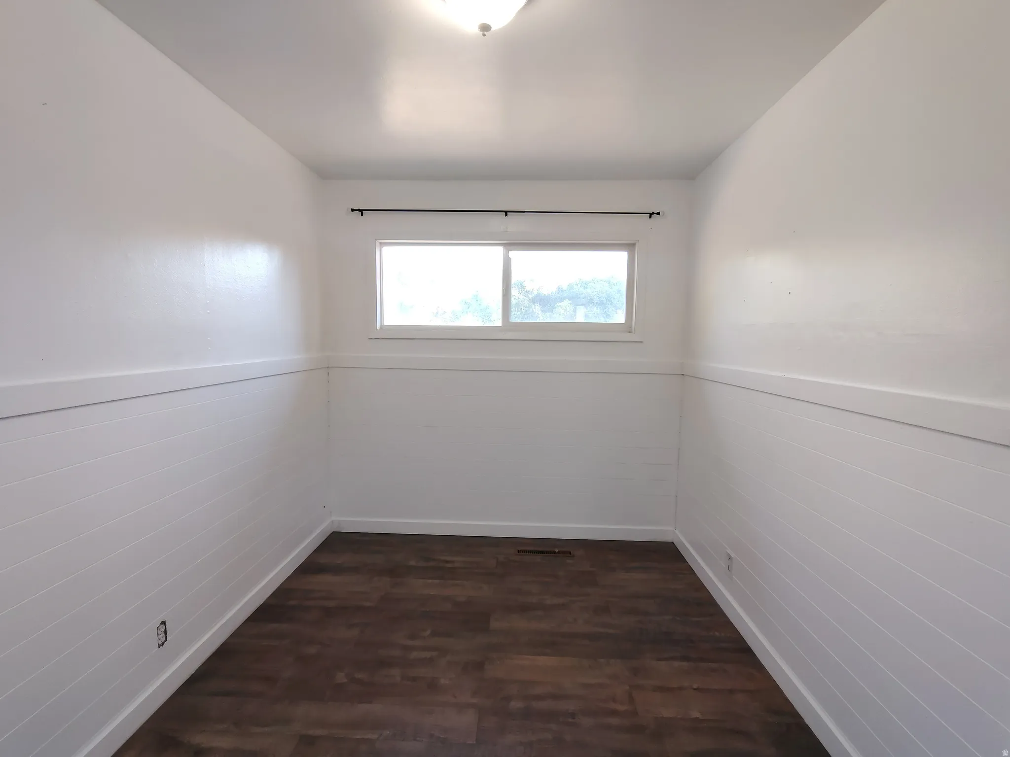 Wood-finish flooring, white shiplap wainscoting, and a window with a dark curtain rod