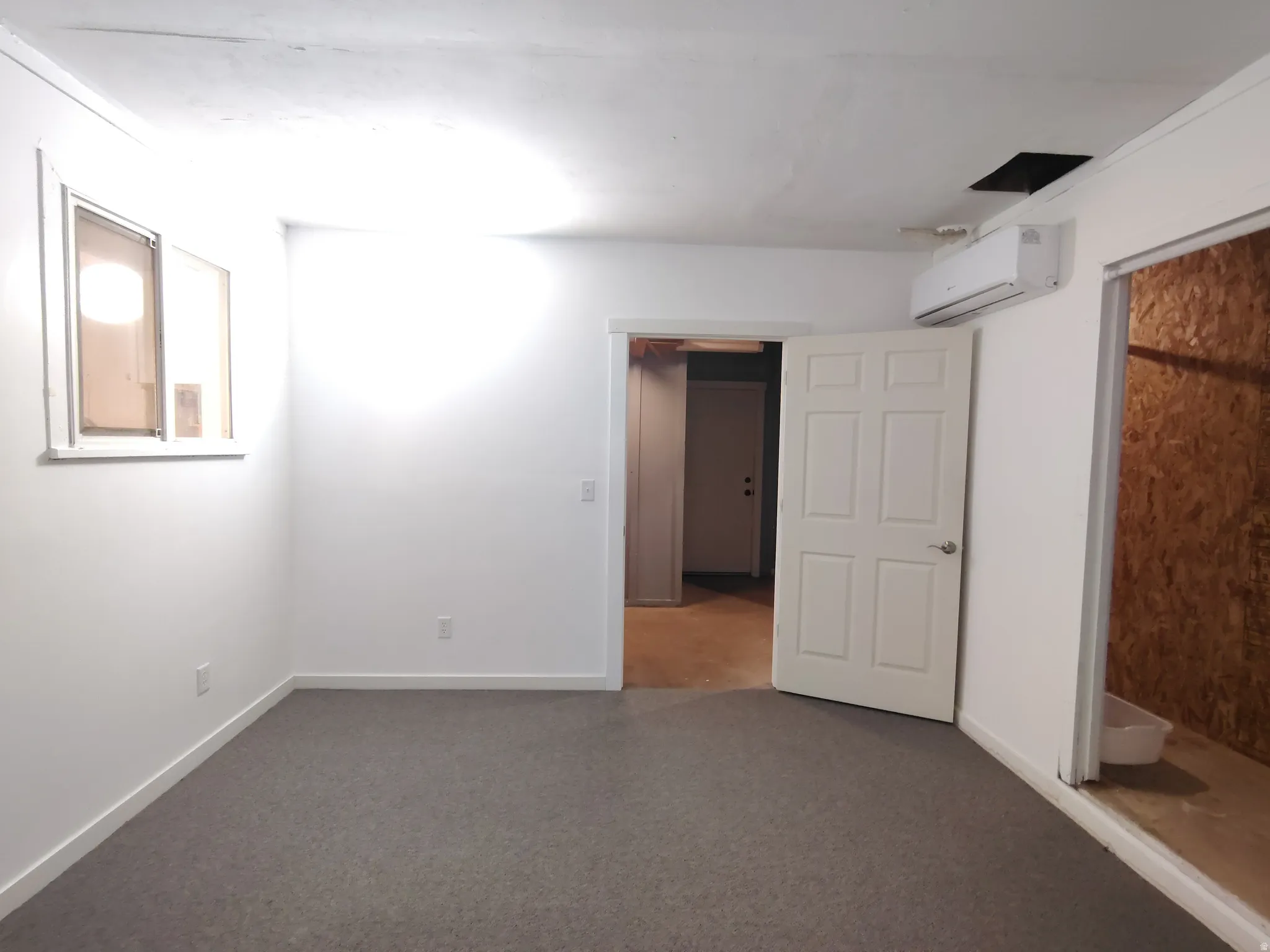White painted walls, gray carpet flooring, and a wall-mounted climate control unit