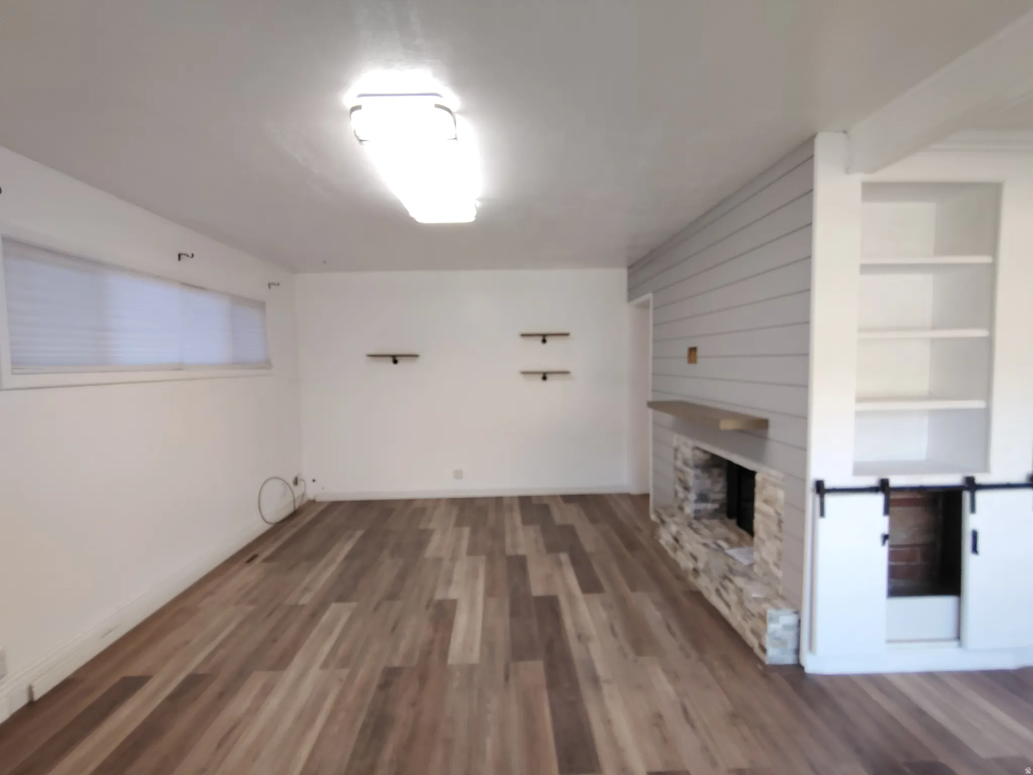Wood-finish flooring throughout, featuring a stone-clad fireplace with a wood mantle, shiplap accent wall, built-in shelving, and sliding barn doors