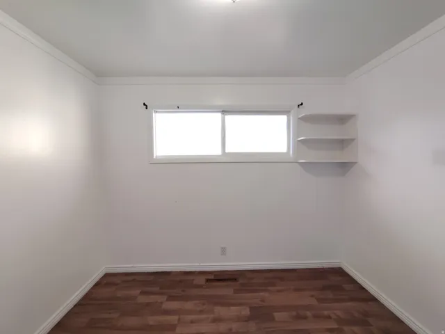 Wood-finish flooring, white walls, crown molding, and built-in shelving