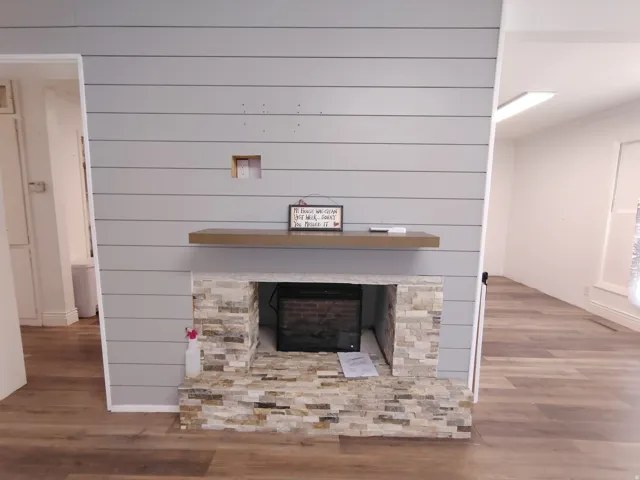 Shiplap accent wall with a stone-clad fireplace and wood-finish flooring