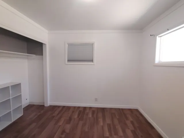 Wood-finish flooring with white baseboards, crown molding, and a built-in closet with shelving