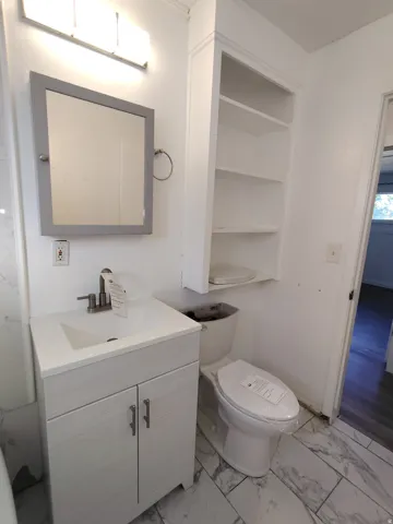 Vanity with integrated sink, wall-mounted mirror, overhead lighting fixture, built-in shelving, and tile flooring