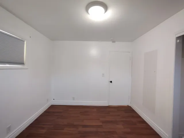 Wood-finish flooring with white baseboards, a single window with blinds, and a flush mount ceiling light