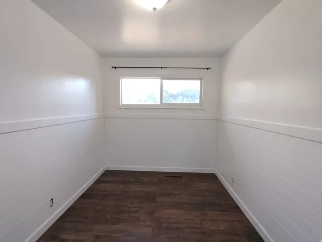 Wood-finish flooring, white shiplap wainscoting, and a window with a dark curtain rod