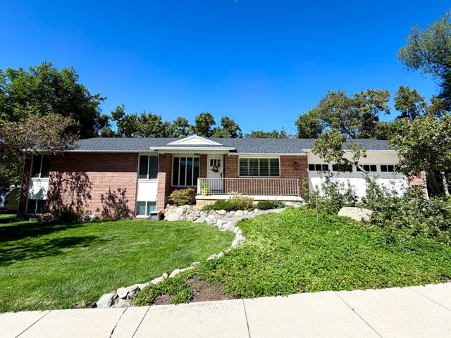 Brick facade residence featuring a front lawn, sidewalk access, white garage door, and a covered entry