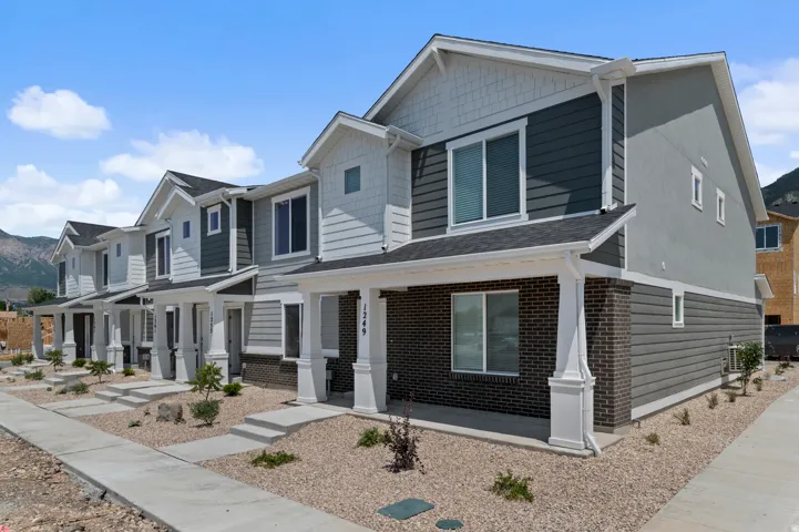 Modern townhome exterior featuring multi-toned siding, brick accents, white trim, a covered porch, and a gravel landscape