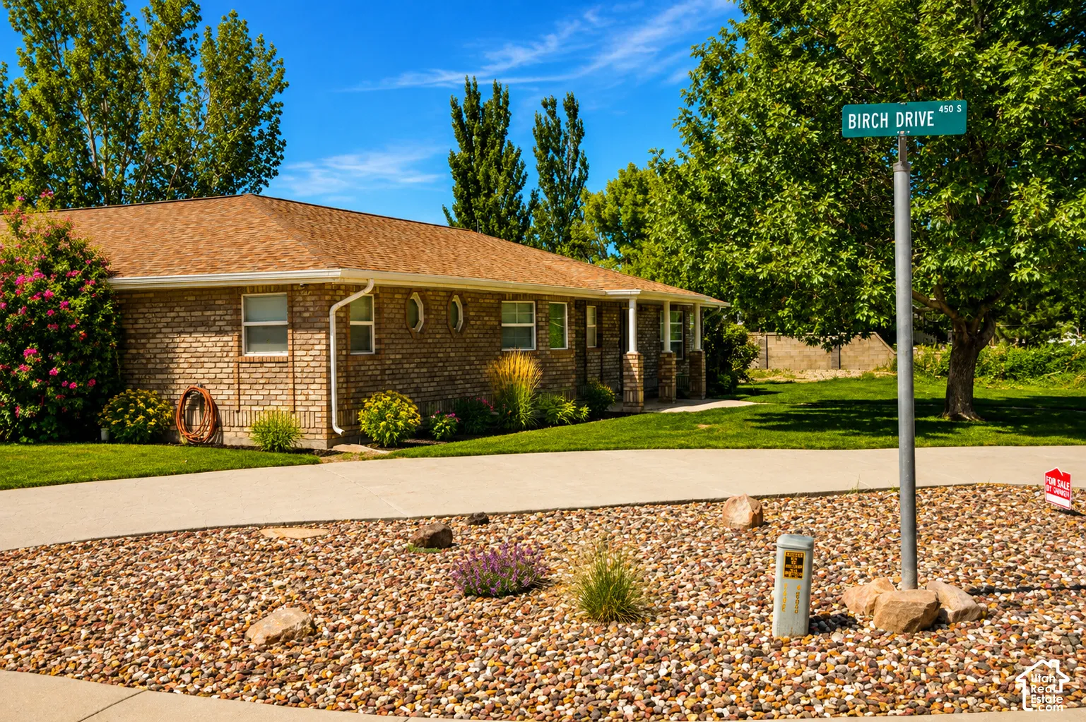 Brick exterior with a brown shingle roof, complemented by mature trees and lush landscaping
