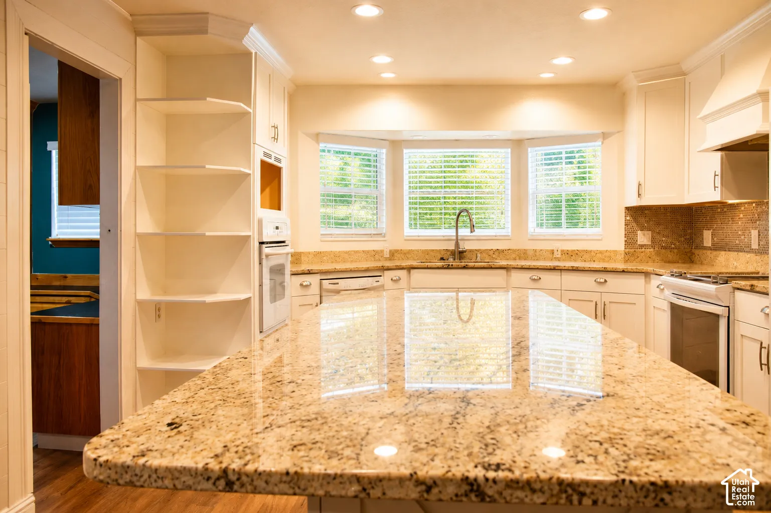 Kitchen featuring a large island with stone countertop, white cabinetry, built-in shelving, and recessed lighting