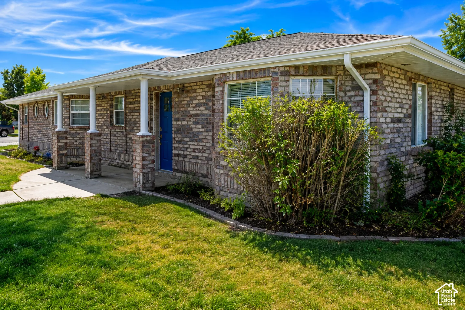 Brick exterior with a covered porch, white columns, blue entry door, and a concrete walkway