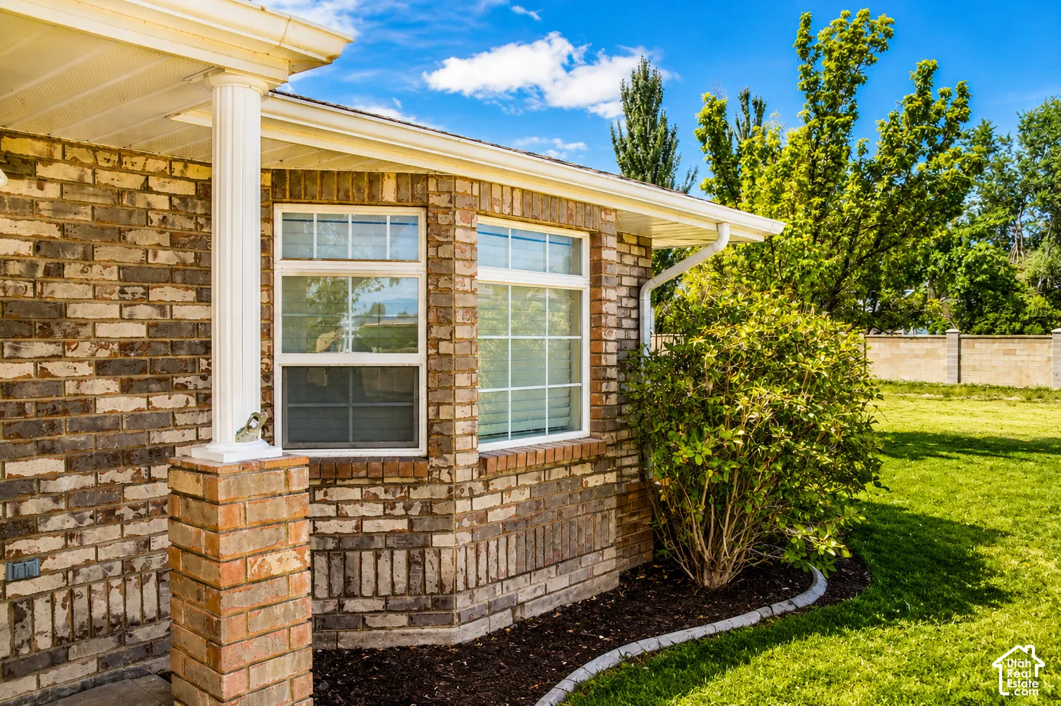 Brick exterior with white window frames, columned entry, and a manicured landscape bed