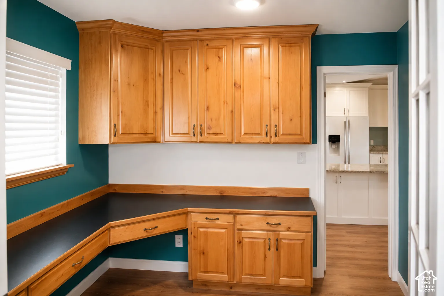 Built-in wood-finish cabinetry with dark hardware, L-shaped desk surface, and wood-finish flooring
