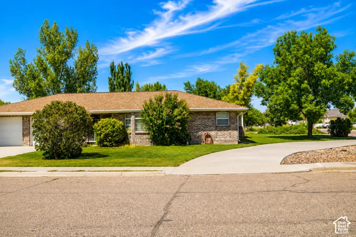 Brick exterior home with an attached garage, a paved driveway, and mature landscaping