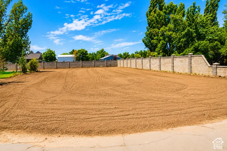 Expansive lot featuring a prepared earth surface, mature perimeter trees, and a substantial block wall