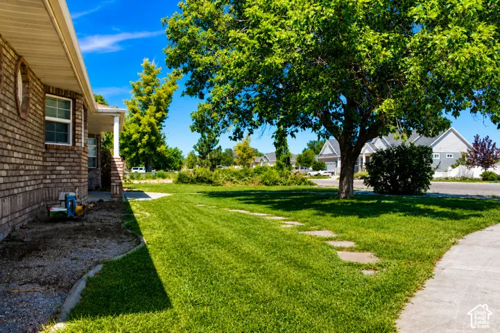 Brick exterior siding with white trim, covered front porch with a white column, mature front yard tree, green lawn, and concrete pathway