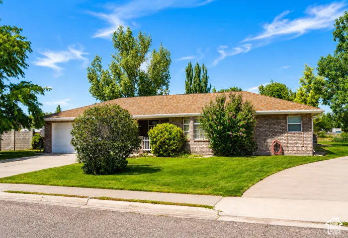 Brick exterior with a shingle roof, attached garage, concrete driveway, and front lawn