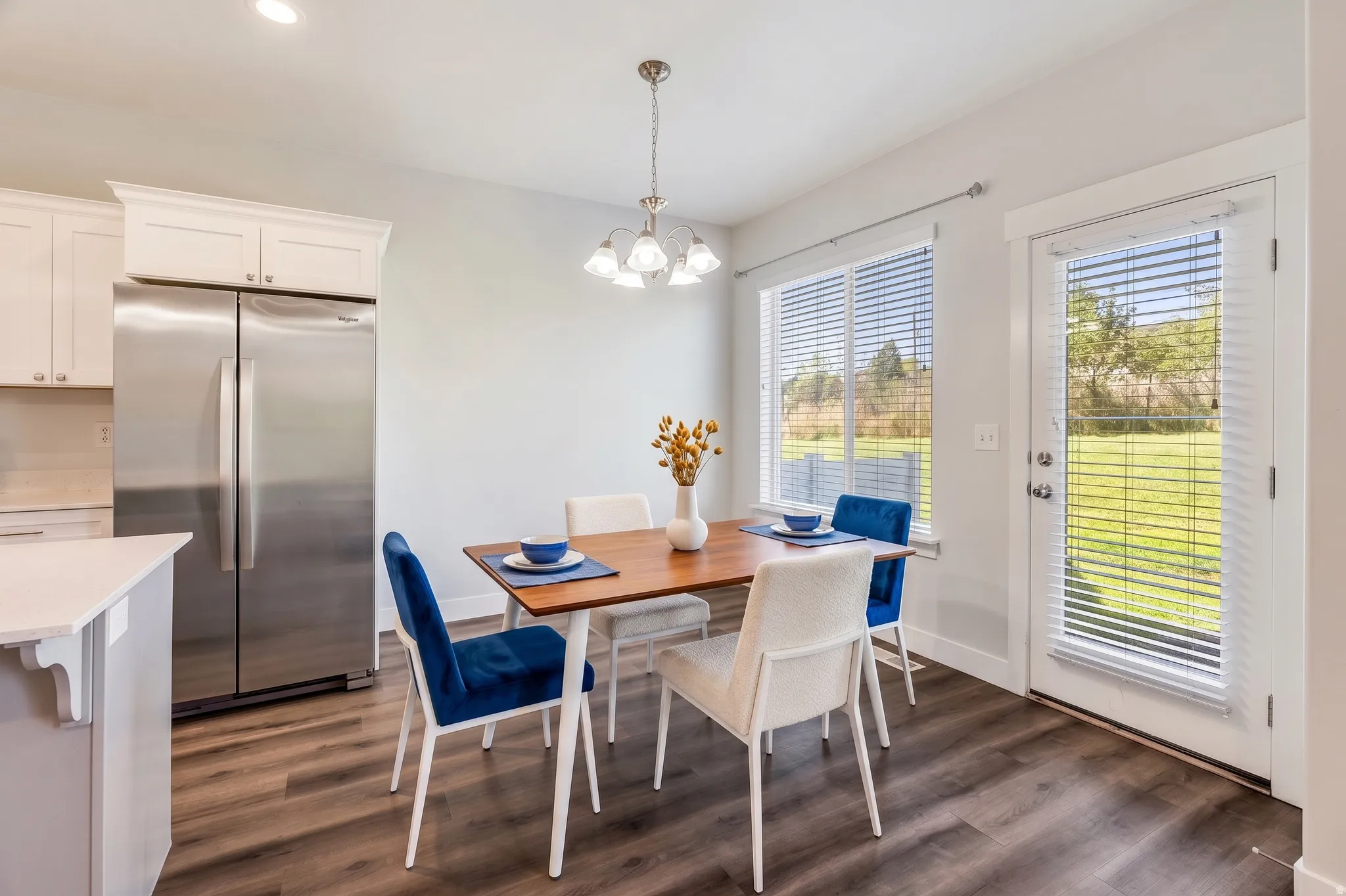 White shaker cabinetry, stainless steel refrigerator, wood-finish flooring, recessed lighting, and a chandelier-style light fixture