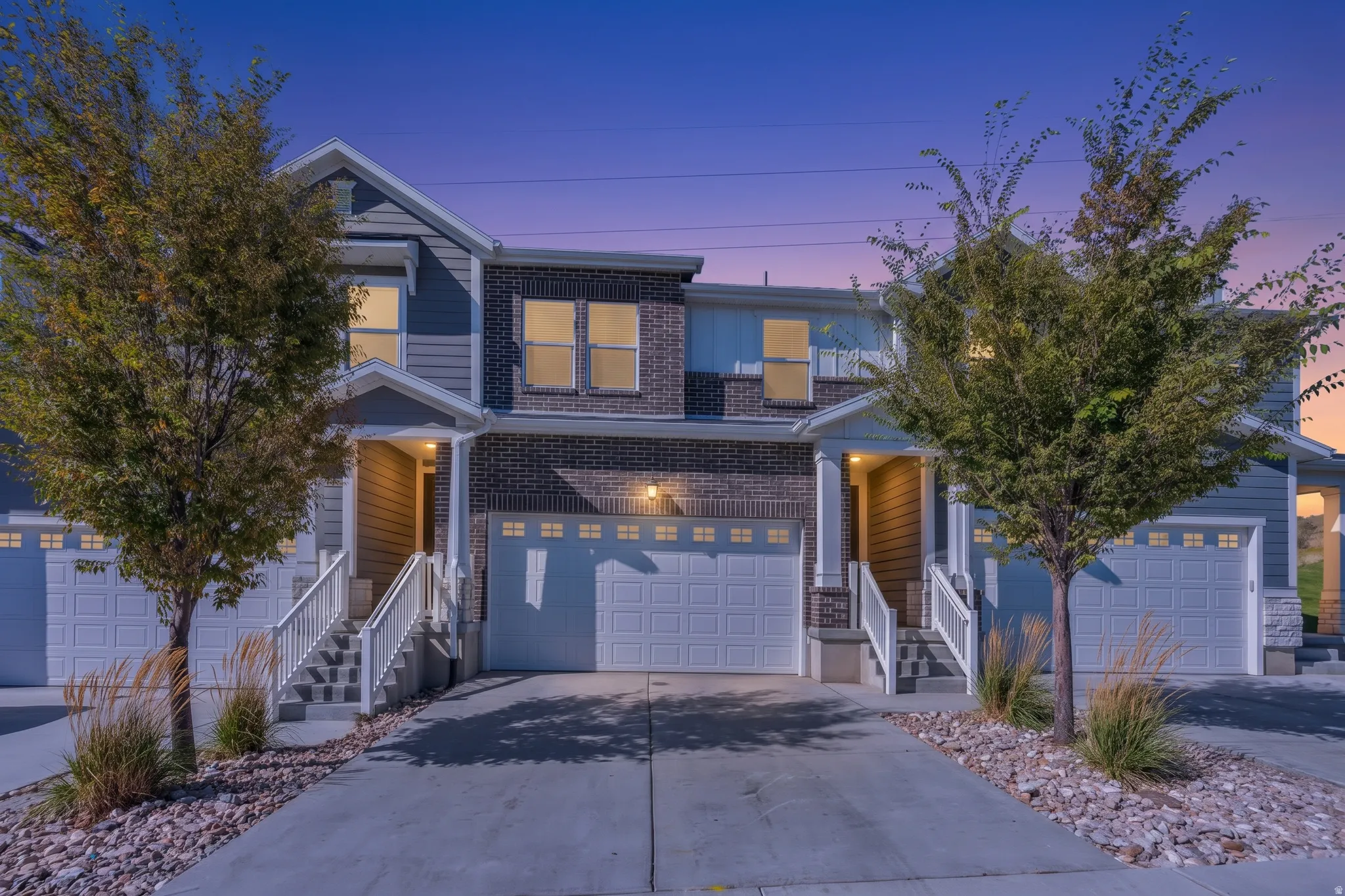 Exterior featuring brick and siding accents, prominent garage doors, and covered entryways with white railings