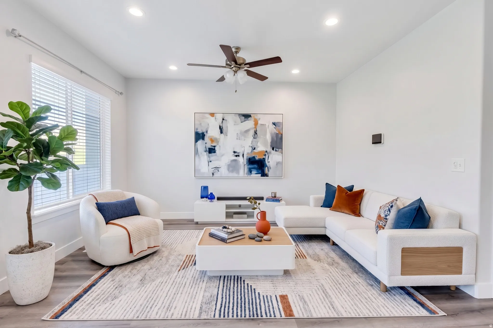 Recessed ceiling lighting, a ceiling fan fixture, large windows, and wood-finish flooring