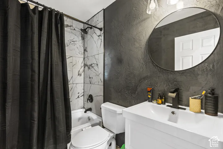 Bathroom featuring a white vanity with integrated sink, a circular mirror, textured dark wall finish, a tub with a tiled surround, and matte black fixtures