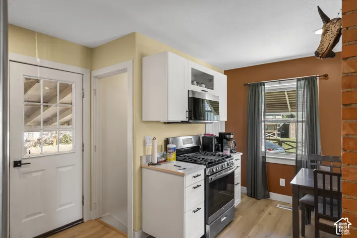 Galley kitchen featuring a gas range, over-range microwave, wood-finish flooring, white cabinetry, and a multi-pane glass door