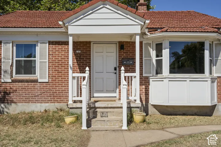 Brick exterior with a covered entry, white paneled front door, bay window, and a terracotta tile roof
