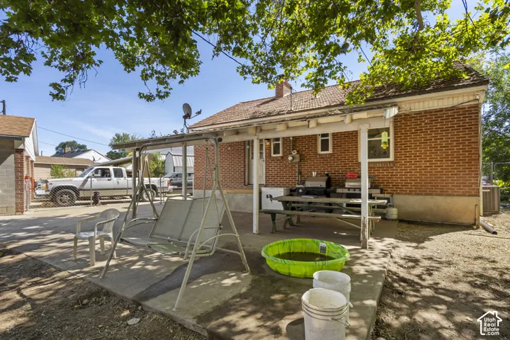Brick exterior home with a covered patio, concrete slab, and mature trees
