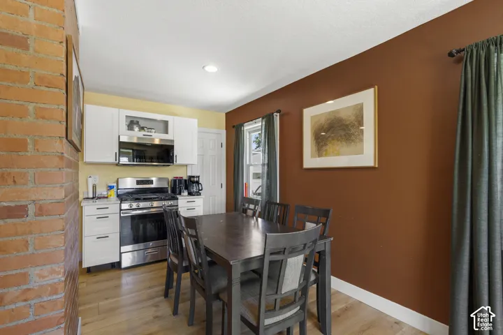 Exposed brick wall detail, light wood-finish flooring, white cabinetry, stainless steel range, and recessed ceiling lighting