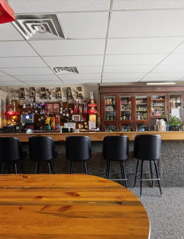 Wood-finish bar with seating for four, built-in display cabinetry, and a textured bar front
