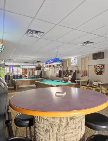 Spacious interior featuring multiple pool tables, a high-top table with bar stools, and a drop ceiling with recessed lighting